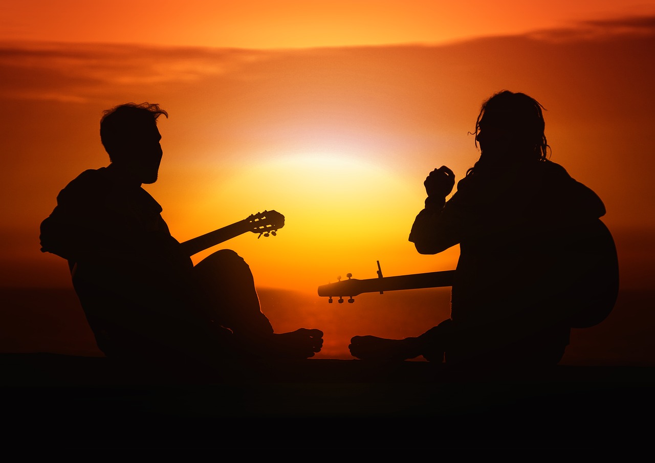 Un homme et une femme qui jouent de la guitare au couché du soleil